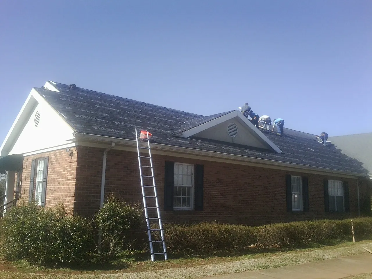 Crew tearing shingles off a brick ranch roof with a ladder set — Emergency Roof Repair work by our crew in Nordland