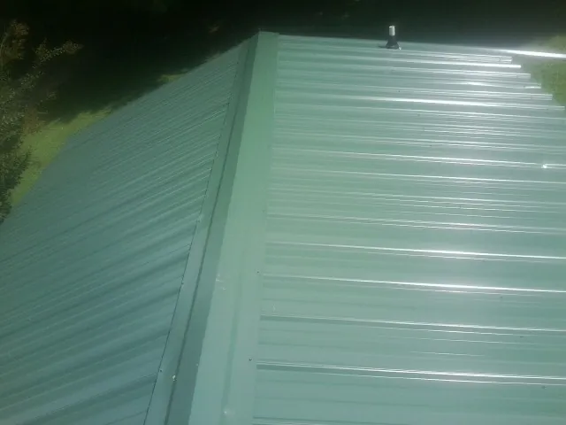 New green metal panels meeting at the ridge of a roof — Flat Roof Repair work by our crew in Nordland