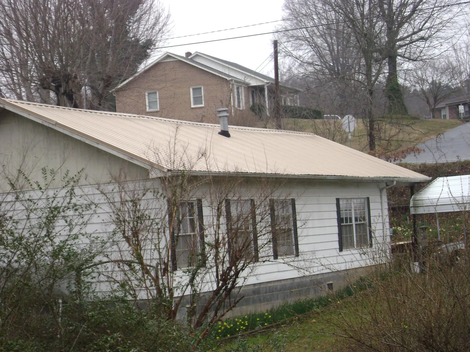 Tan metal roof on a white sided house set into a hillside — Commercial Roofing by Roofing Brothers in Nordland