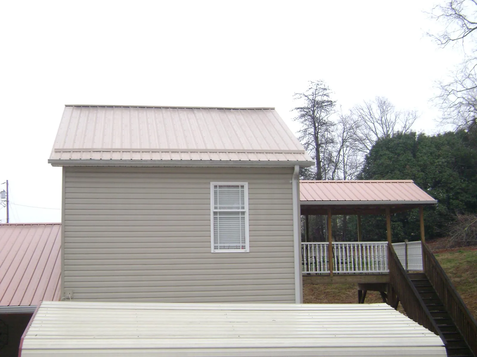 Tan metal roofs on a two story addition and attached porch, from a Roof Replacement job in Nordland